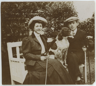 112-0001 Man en vrouw met hond in een tuin op houtenbankje, 1880-1940