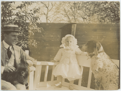 112-0022 Man met kind en twee honden in een tuin op een houtenbankje, 1880-1940
