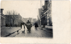 418 Prentbriefkaart met echte foto van de Grotestraat te Borne. Op straat wandelen een man en vrouw met kinderwagen. ...