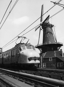 151895 Afbeelding van een electrisch treinstel mat. 1954 van de N.S. op het spoorviaduct te Delft, met rechts de molen ...