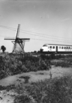 151022 Gezicht op een molen en een passerend electrisch treinstel mat. 1964 (plan V) van de N.S. ter hoogte van Hazerswoude.