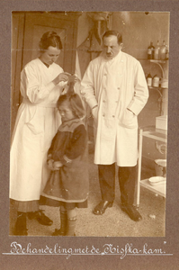26143 Afbeelding van een meisje tijdens de behandeling met de Nisfka-kam (ontluizen). Rechts staat de gemeentearts dr. ...