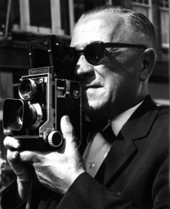 125206 Portret van de Utrechtse fotograaf L.H. Hofland (1909-1987) met zijn tweeoogs Mamiyaflex-camera.