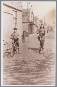 WAT002000780 Links Maarten Schoenmaker (1926) en zijn moeder Lotje Langenberg (1892) op de fiets voor de winkel van ...