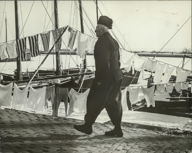 NNC-63-1139-01 Volendammer loopt op een maandag in de winter langs de haven.