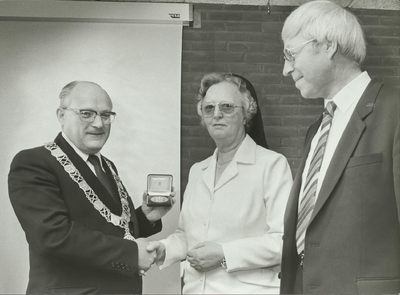 NNC-84-87-01 Burgemeester Westendorp (links) overhandigt de ere-penning van de gemeente aan zuster Marie Dominique, de ...