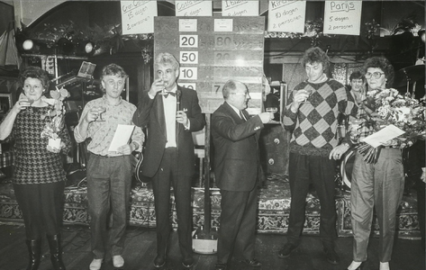 NNC-86-275-01 Presentator Kees Machielsen en burgemeester Westendorp heffen het glas met een aantal prijswinnaars van ...