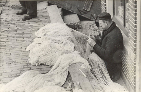 WAT006002465 Dirk Kwakman 'Dirk Bol' met z'n rug tegen de gevel van de winkel van Bart Koning, bezig met herstellen van ...