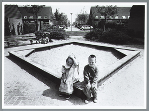 WAT001010335 Verschonen van de zandbak.Twee kleuters zitten op de rand van de zandbak. Tussen de woningen aan de ...