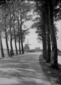 162 Opname van de weg naar Windesheim, met een molen en een kerkje op de achtergrond. Op straat rijdt een fietser., ...