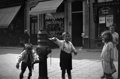 257 Straatbeeld: spelende kinderen bij waterpomp, voor Kaas Visch en - en Fruithandel van Bloemink aan de Brink. Rechts ...