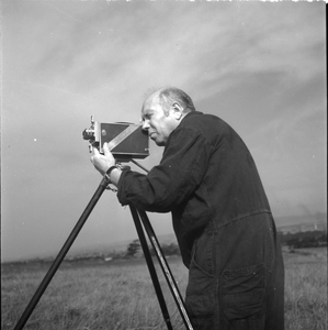 263 Alex Roosdorp aan het werk, filmend achter zijn camera in een weiland. Lokatie onbekend., 01-01-1920 - 01-01-1960