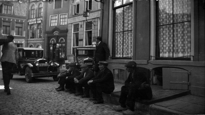 289 Grote Kerkhof, voor Hotel de Engel en de winkel van Kruidenier C.H. Horst. Heren met pet zitten te wachten op de ...