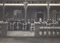 15 Leraren en leerlingen van het gymnasium te Doetinchem, gezeten op een terras van een horecagelegenheid onder een ...