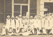 24 Groepsfoto van leerlingen (meisjes) in uniform van de Modevakschool Doetinchem, poserend voor de gevel van de school