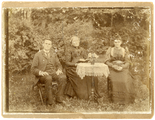 13-0021 Een man, een oudere vrouw en een jonge vrouw aan een tafel in een tuin, 1900-1920