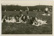18 Jongeren liggen in het gras terwijl op de achtergrond wordt gevoetbald, 1928-1935