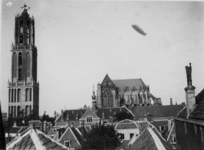 82108 Gezicht op de Domkerk en de Domtoren (Domplein) te Utrecht; vanuit het zuiden met in de lucht het luchtschip Graf ...