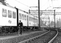 153326 Afbeelding van een beambte van de spoorwegpolitie op de fiets op het emplacement te Amsterdam C.S.