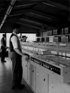 156465 Afbeelding van een seinhuiswachter bij het 120-voudig stelknoptoestel in het seinhuis post A van het ...
