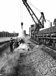 164317 Afbeelding van het plaatsen van een betonnen voet voor een bovenleidingsmast langs de spoorlijn tussen Breda en ...
