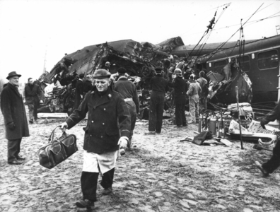 157519 Afbeelding van een reddingswerker met een stuk bagage van een slachtoffer van de treinramp te Harmelen. Op de ...