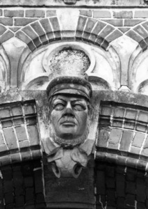 155124 Afbeelding van een sluitsteen met een gebeeldhouwde kop van een boer boven een arcade van het N.S.-station ...