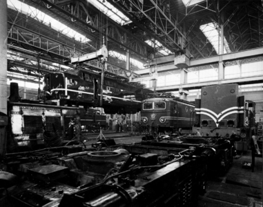 156531 Gezicht in de revisiehal van de hoofdwerkplaats van de N.S. te Tilburg met links in de takels de bak van de ...