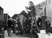 94164 Afbeelding van een aantal bewoners van een woonerf te Maartensdijk, bezig met het optuigen van een kerstboom.N.B. ...