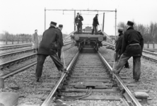 167437 Afbeelding van wegwerkers van de N.S. tijdens het lossen van spoorstaven op de spoorlijn nabij Putten.