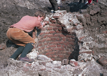 827207 Afbeelding van een archeoloog tijdens het blootleggen van een gemetselde put op het terrein aan Achter ...